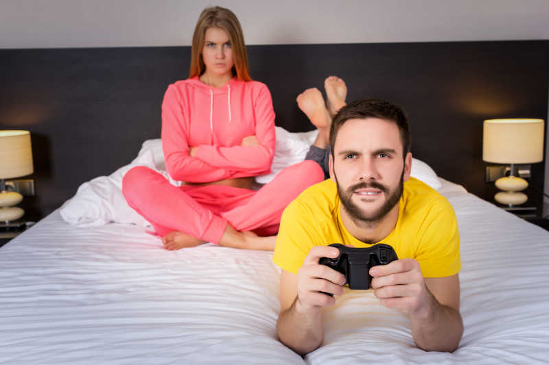 床上玩游戏的丈夫以及生气的妻子