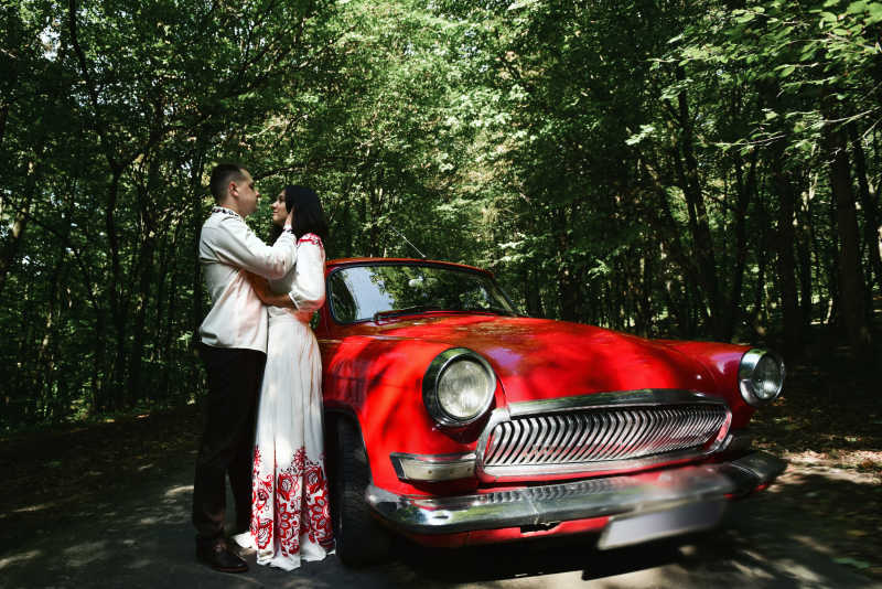 红色复古汽车旁边对视的新郎和新娘