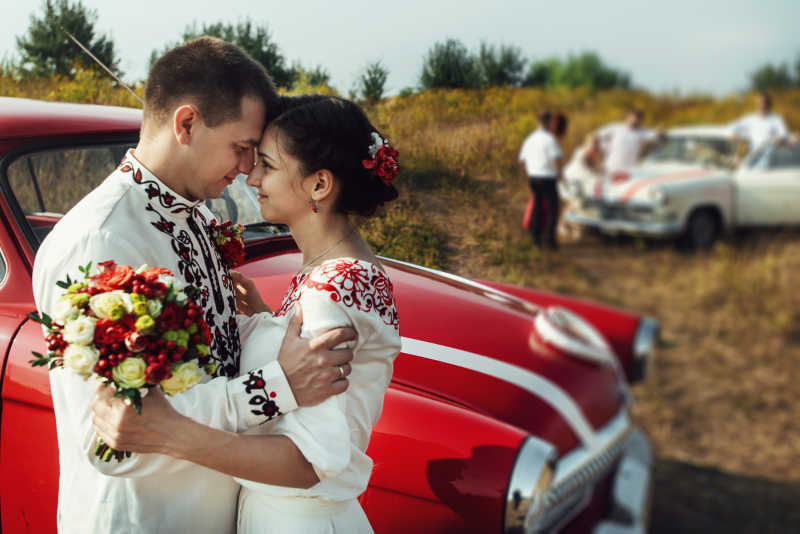 新郎和新娘亲昵的站在红色复古汽车旁边