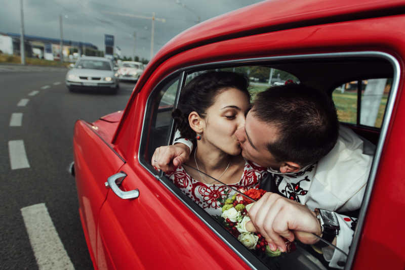 红色汽车里亲吻的新郎和新娘