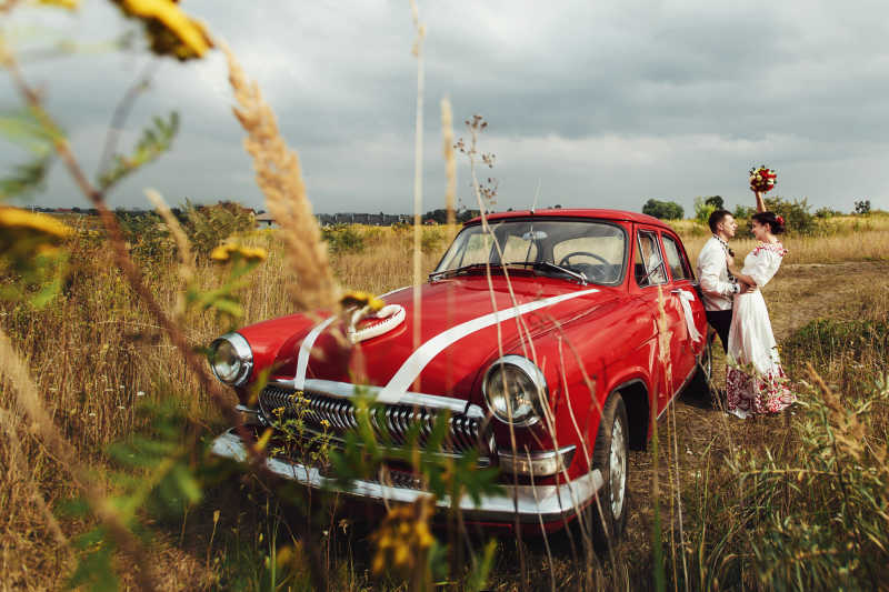 红色复古汽车旁边的新娘和新郎