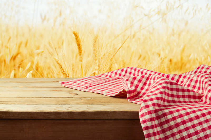 金色麦田背景下的木桌上放着红色格子台布