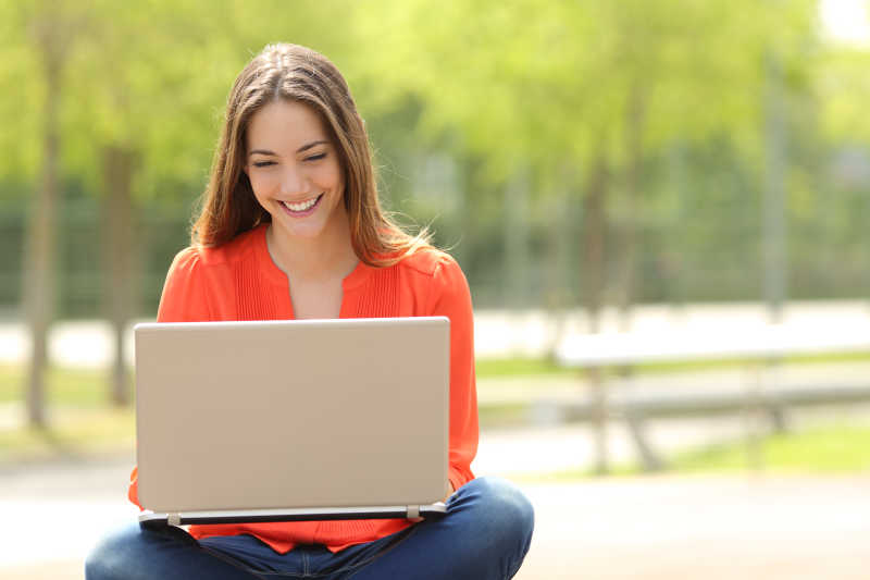 绿色公园里使用笔记本电脑视频聊天的女孩