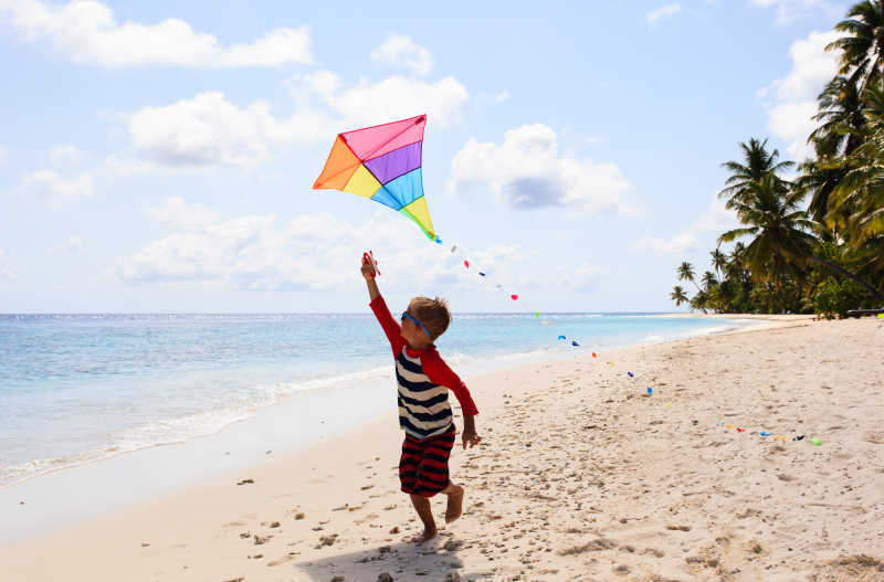 在热带海滩上放风筝的小男孩
