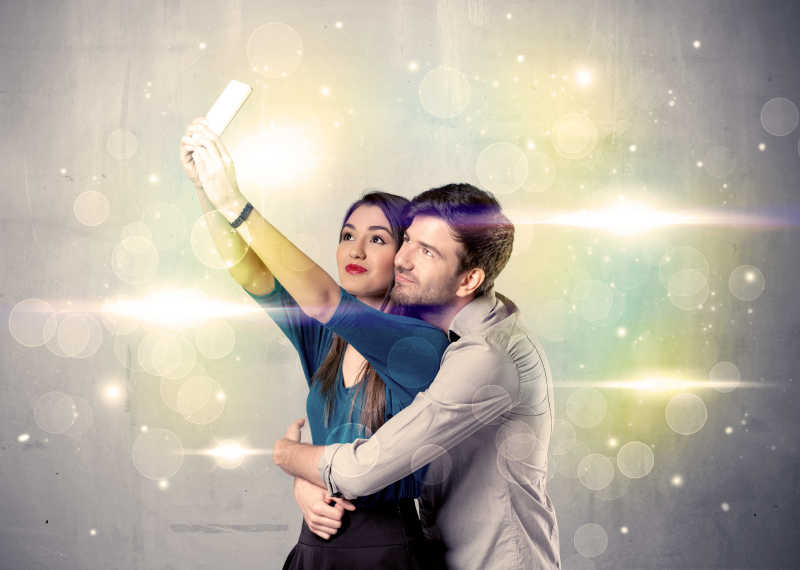 幸福的夫妇在彩灯闪烁背景前拿着手机自拍