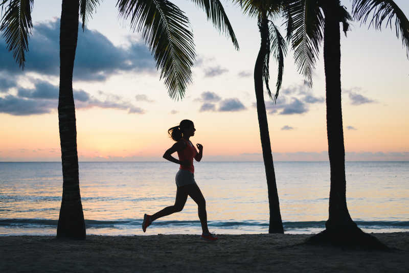 黄昏时分在热带沙滩上跑步的年轻女孩