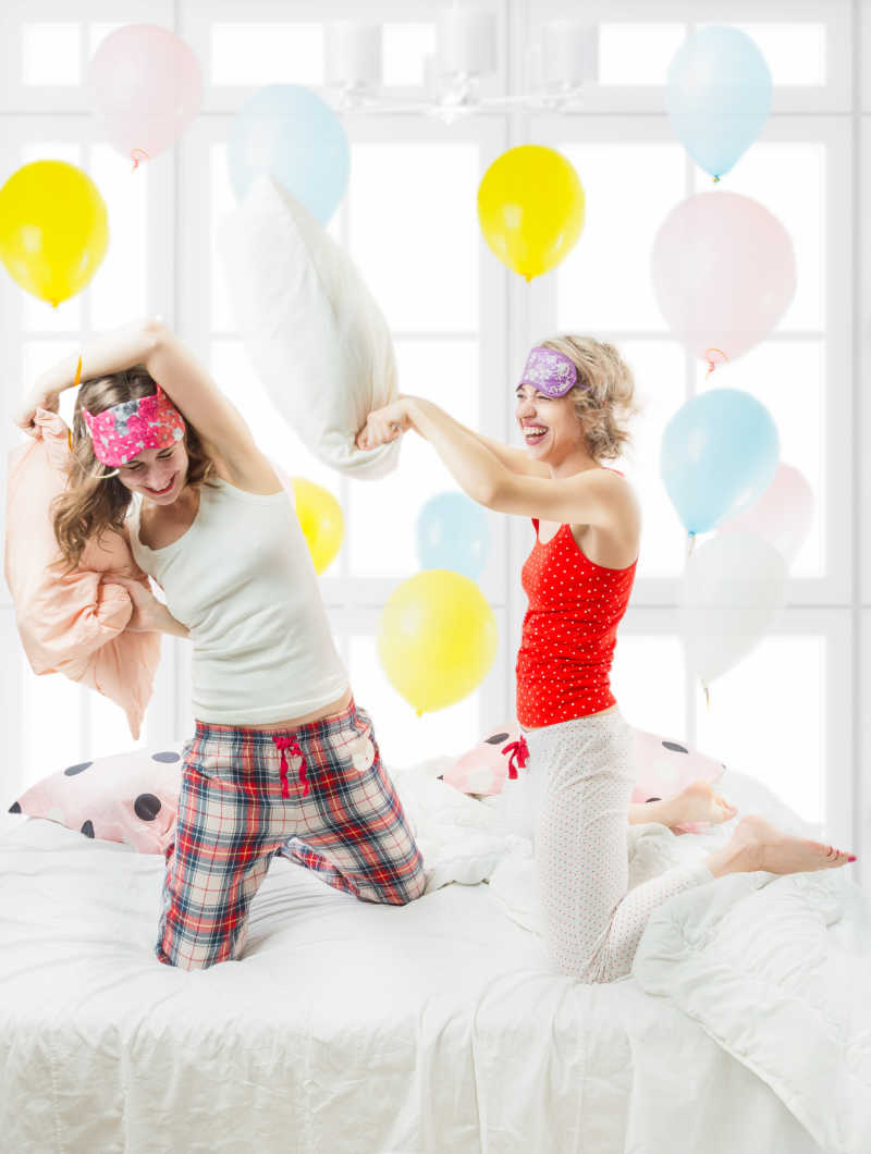 两个女孩在卧室里开心的玩着枕头大战