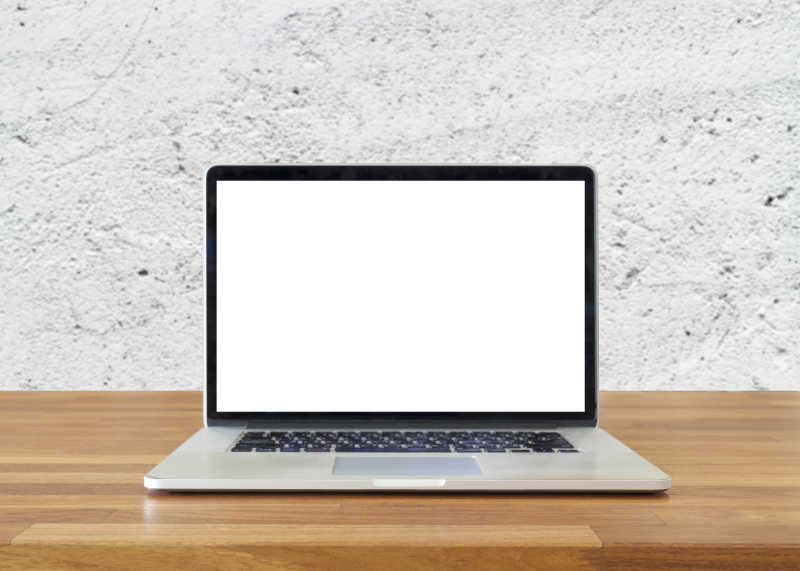 白色水泥墙前木桌上的空白屏幕笔记本电脑
