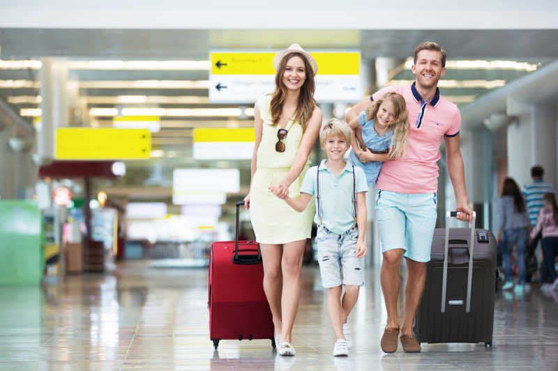 在机场拉着手提箱的幸福家庭