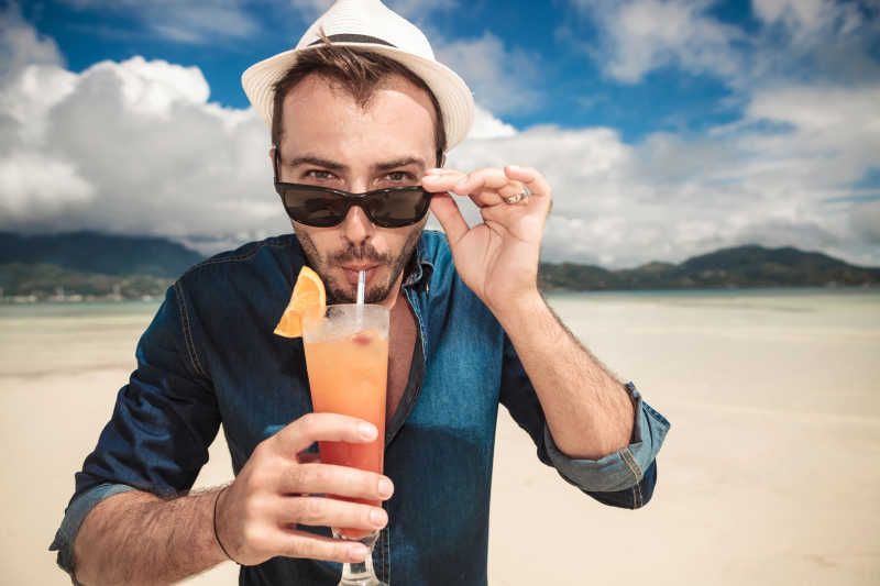 男子在海滩上喝着橙色鸡尾酒
