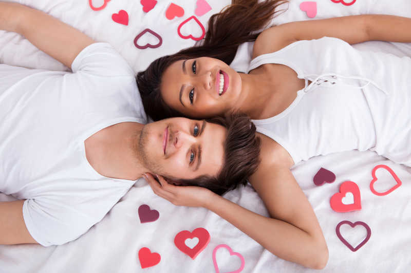 一对夫妇躺在满是心形纸片的床垫上