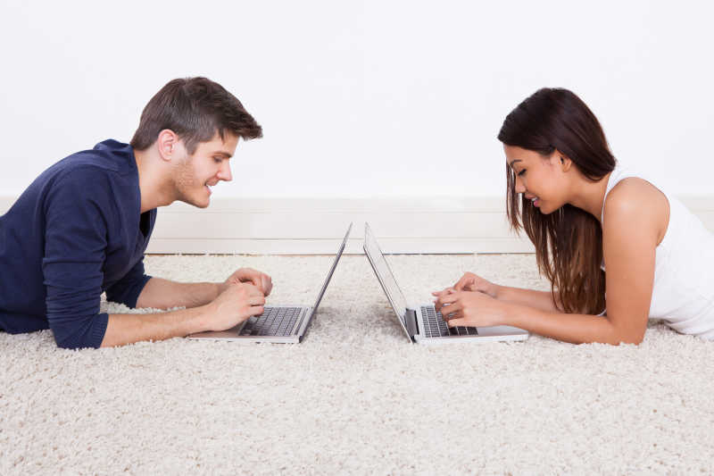 相对趴在白色地摊上使用笔记本电脑的夫妇