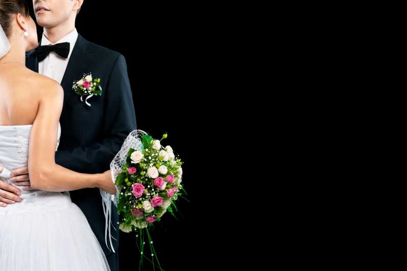 黑色背景下拿着花束的幸福的新郎和新娘