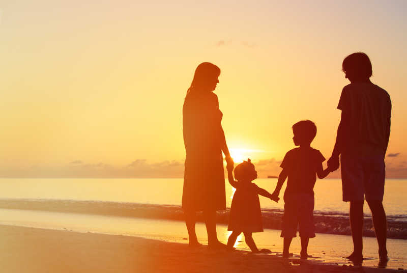 日落时分海滩上有两个孩子的幸福家庭