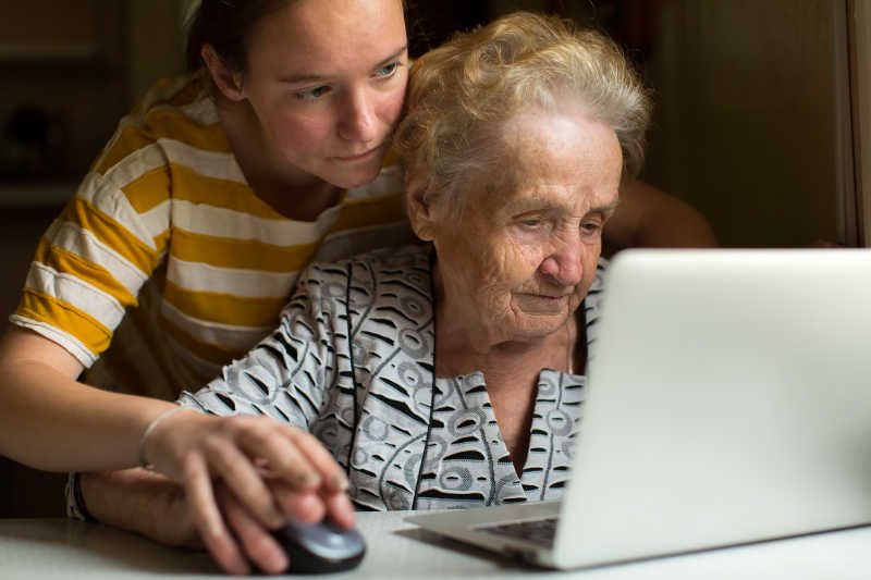 在笔记本电脑前小女孩教给老奶奶使用电脑