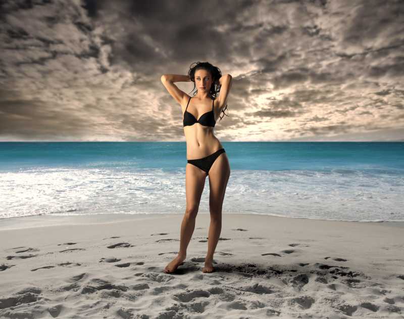 有云的天空下海边沙滩上穿着黑色比基尼的美女
