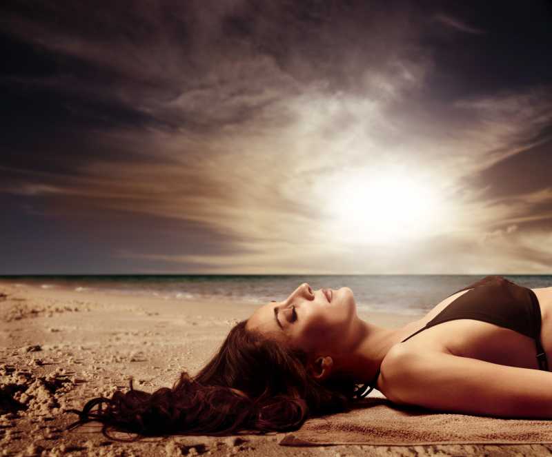 日落背景下穿着比基尼躺在沙滩上的美女