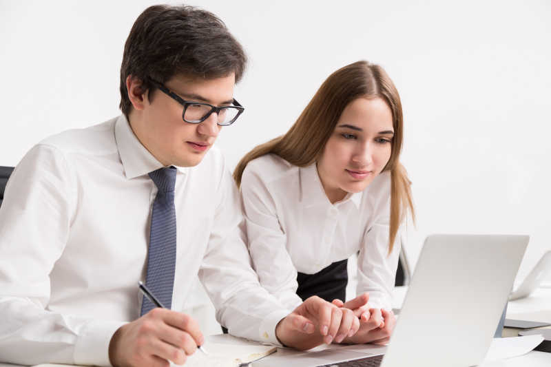 年轻的微笑的老板和女同事看着笔记本电脑