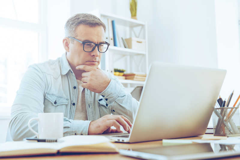 戴眼镜的男人坐在电脑桌前思考工作