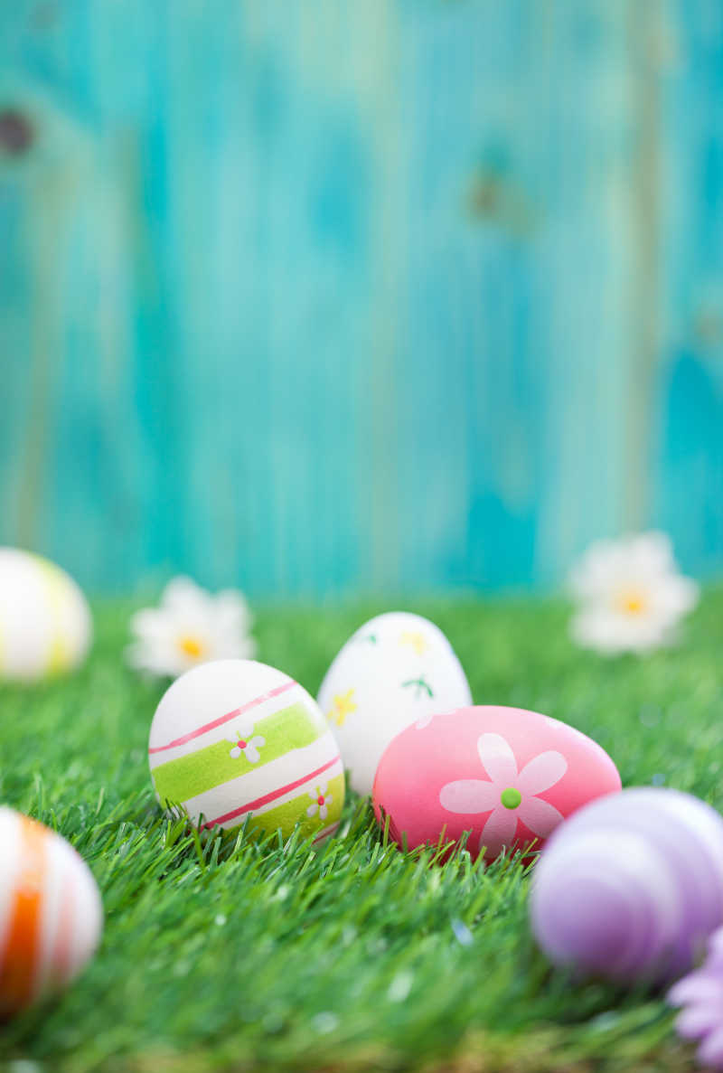 蓝色木板背景下绿色草地上的复活节彩蛋