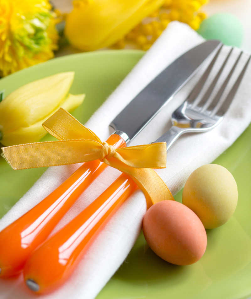 黄色花朵背背景下的复活节餐桌上的餐具和彩蛋