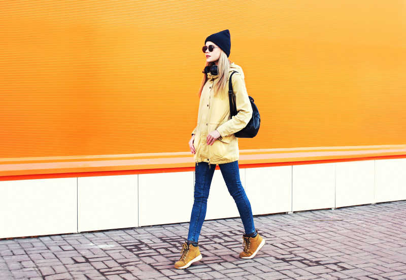 在橙色墙面前散步的金发女孩