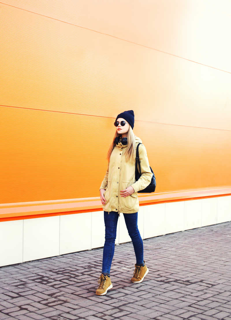 在橙色墙面前散步的时尚美女