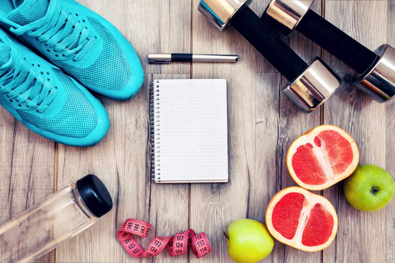 木桌上的健身器材水果运动鞋和笔记本