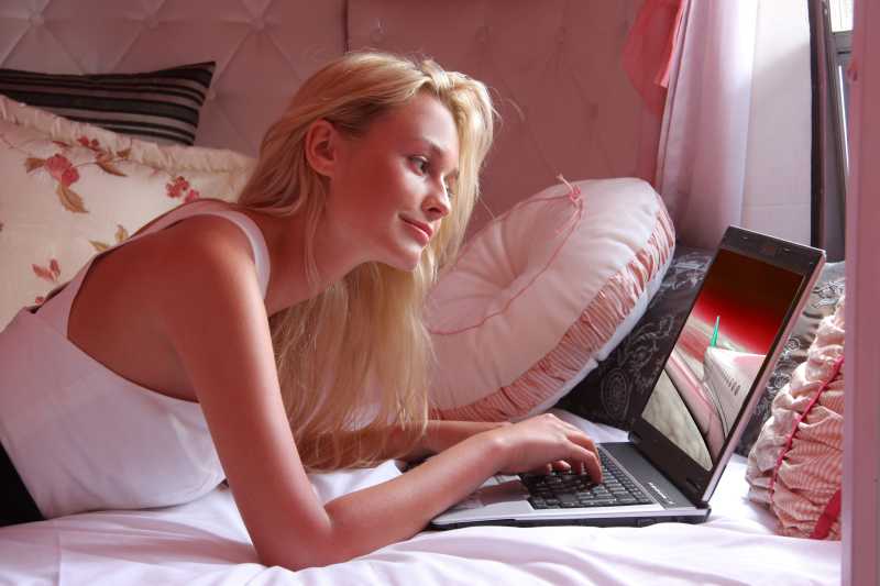 趴在床上使用笔记本电脑的金发美女