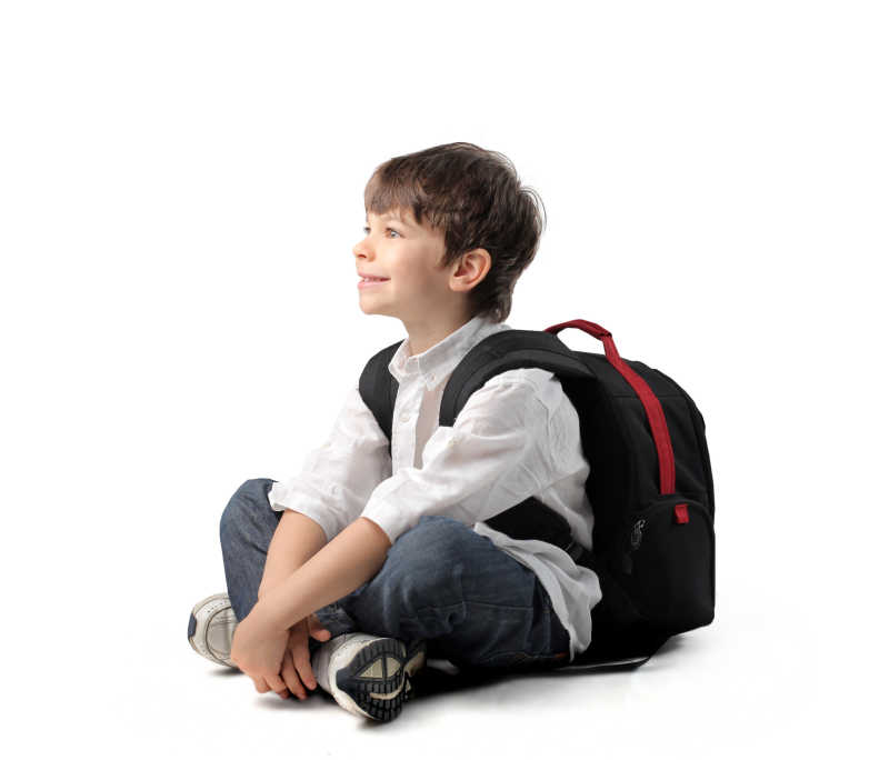 小男孩背着书包微笑的坐在地上
