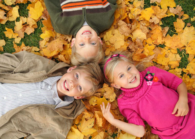 躺在户外秋叶上的三个可爱小孩