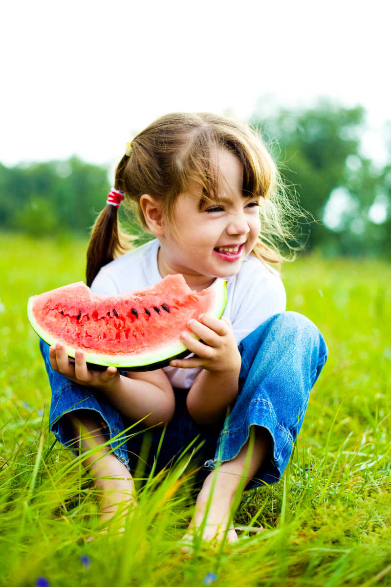 可爱的小女孩在草地上吃西瓜
