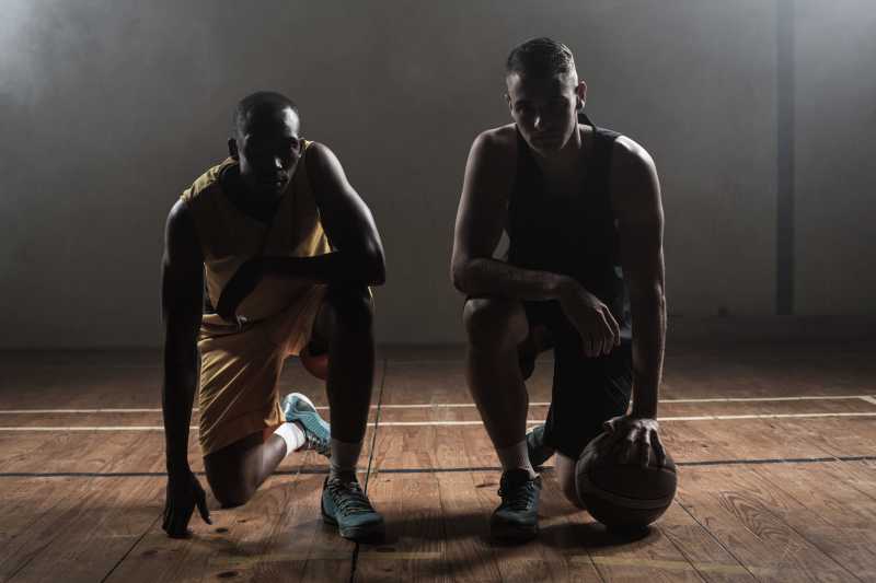 体育馆里跪在地上的两位篮球运动员手拿篮球