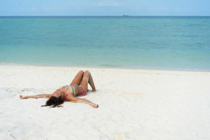 蓝色海边躺在白色沙滩上穿着比基尼的美女