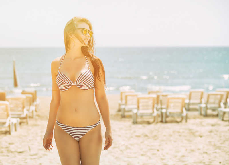 阳光下沙滩上穿着比基尼戴着太阳镜的美女