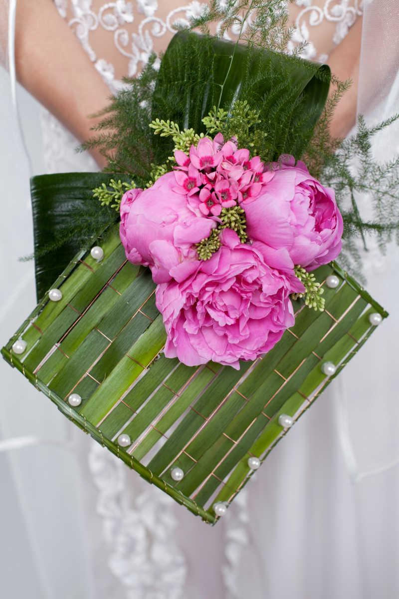 新娘手中的绿色叶子的粉色的结婚花束