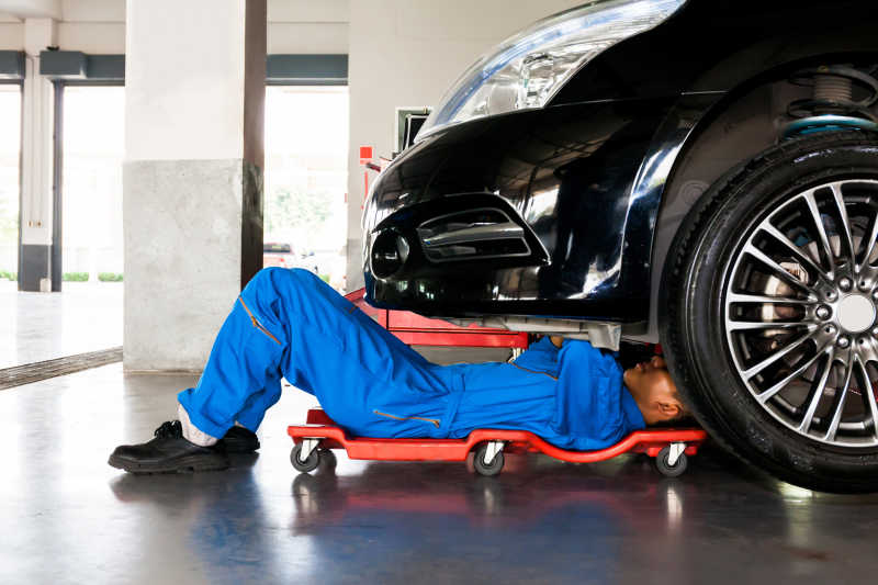 汽车修理厂里穿着蓝色制服的机修工躺在汽车下边工作