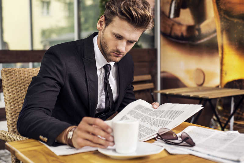穿着西装边看报纸边喝咖啡的男人