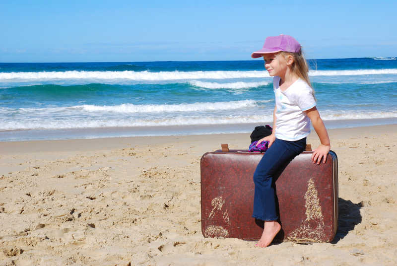 沙滩上坐在旅行箱上的小女孩