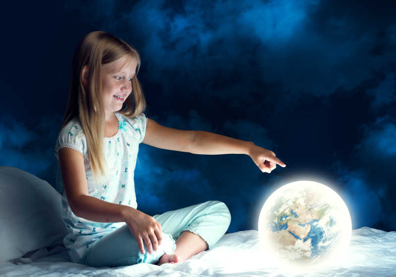 女孩在她的床上指着发光的地球仪