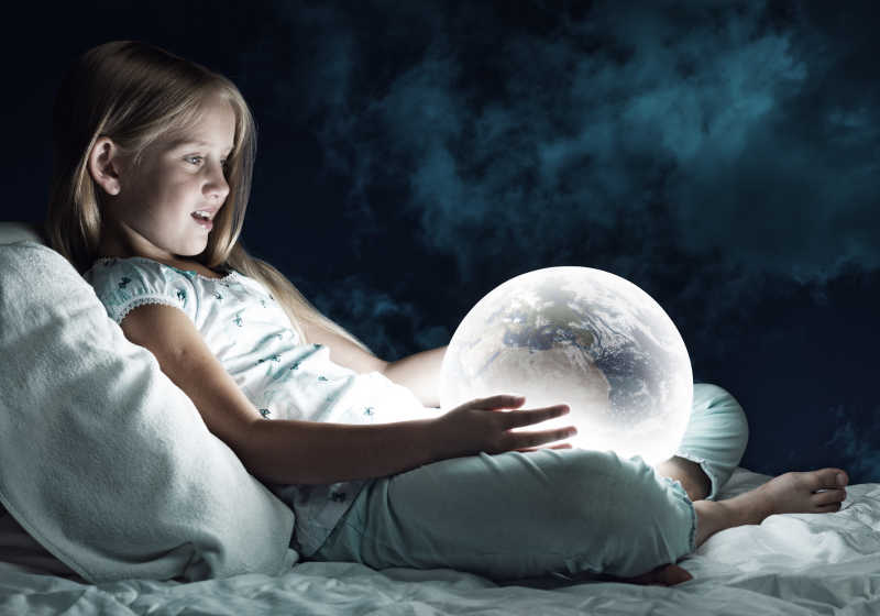 女孩在她的床上看发光的地球仪