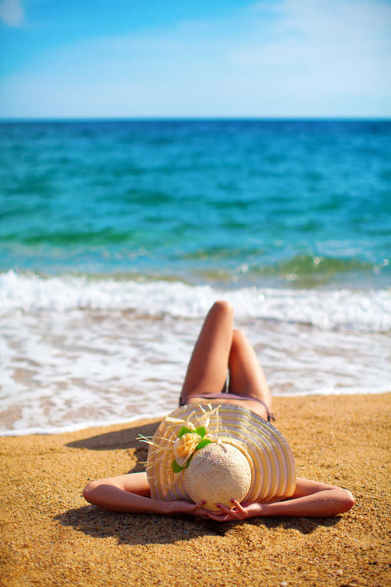 戴着草帽躺在沙滩上的比基尼美女