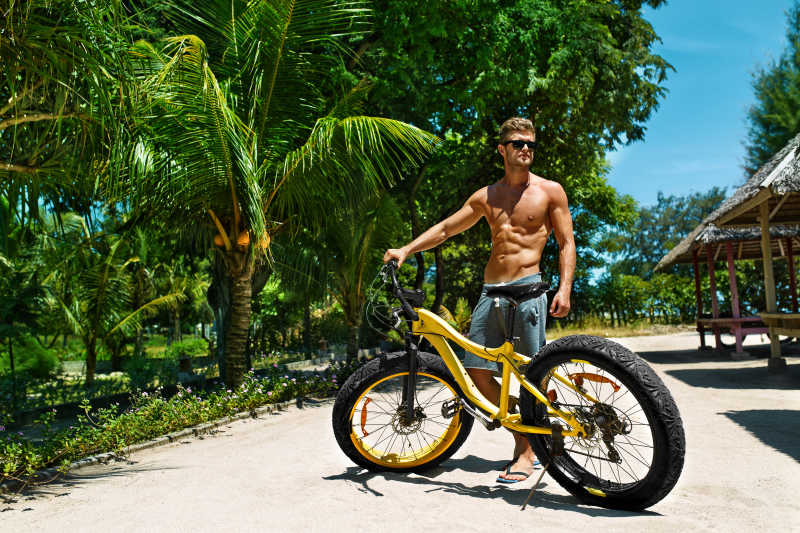 戴太阳镜的帅哥在热带海滩骑自行车