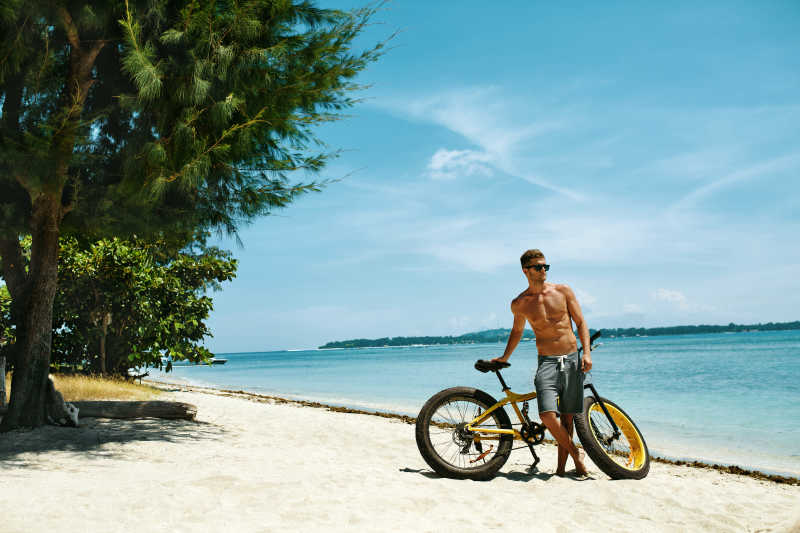 健身帅哥骑黄色自行车在海边太阳晒