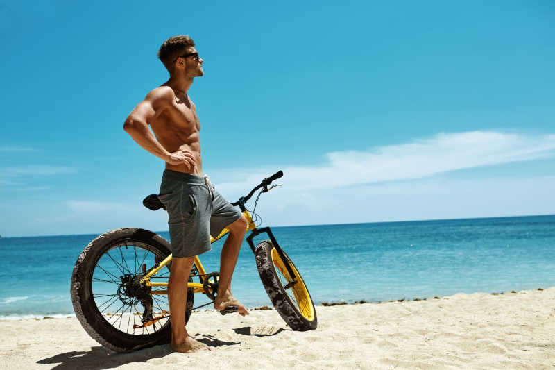 健身男模特骑黄色自行车在海边晒太阳