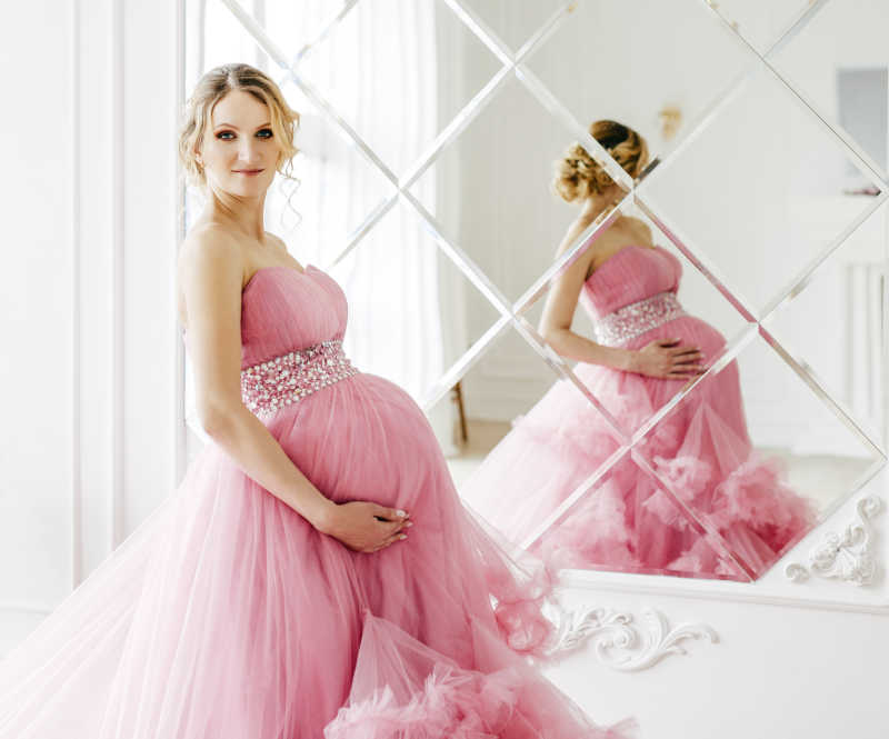 美丽孕妇穿着粉红色华丽连衣裙