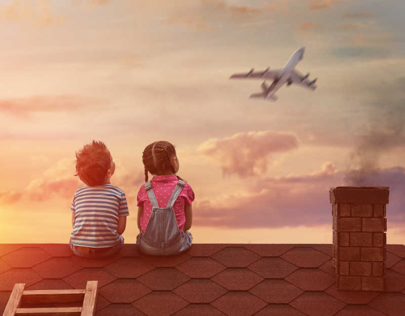 两个小孩在屋顶上坐着看着天空上的飞机