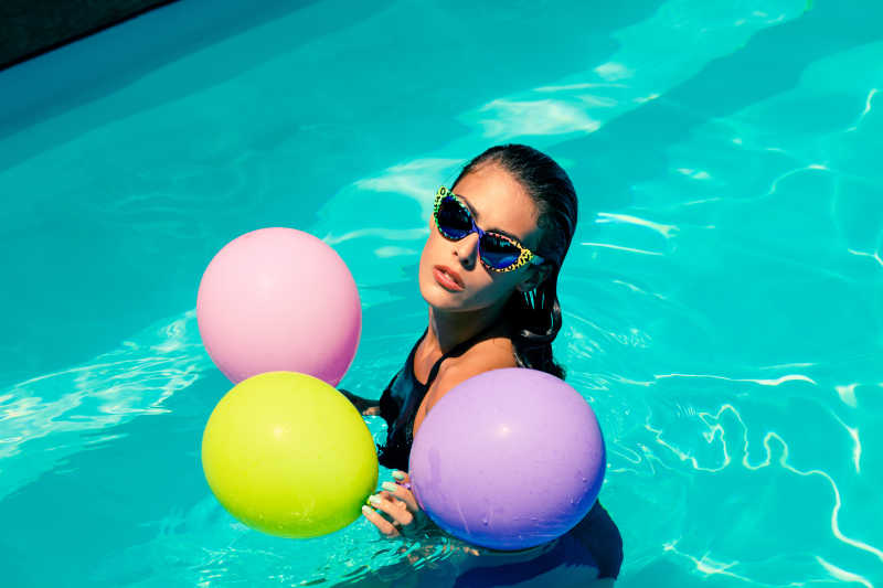 游泳池里有太阳镜和气球的年轻漂亮女人
