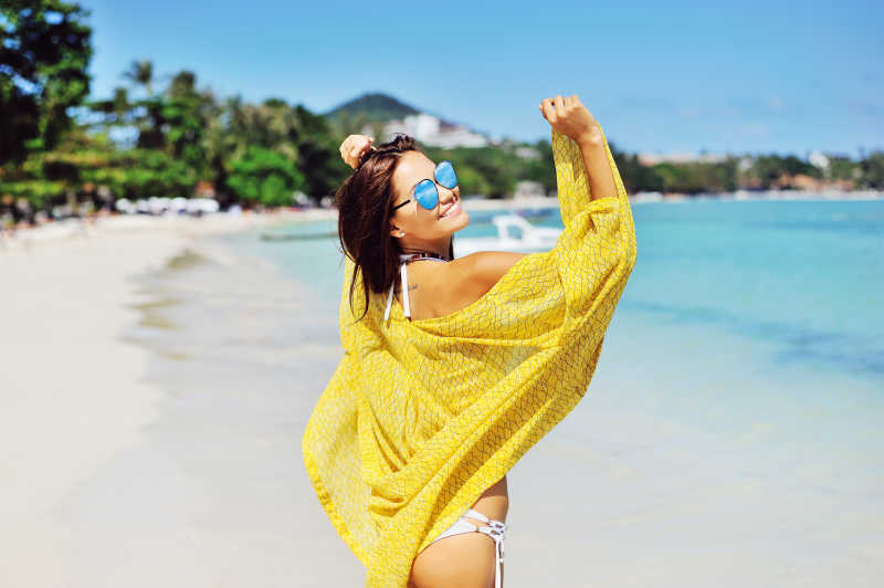 蓝天下沙滩上穿着白色比基尼披着黄色防晒衫的美女