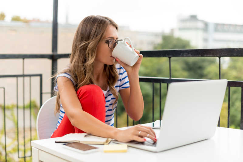 室外背景下在家使用电脑办公时喝咖啡的美女